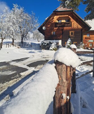 The snowy farmhouse with a wooden balcony and a snow-covered wooden fence.