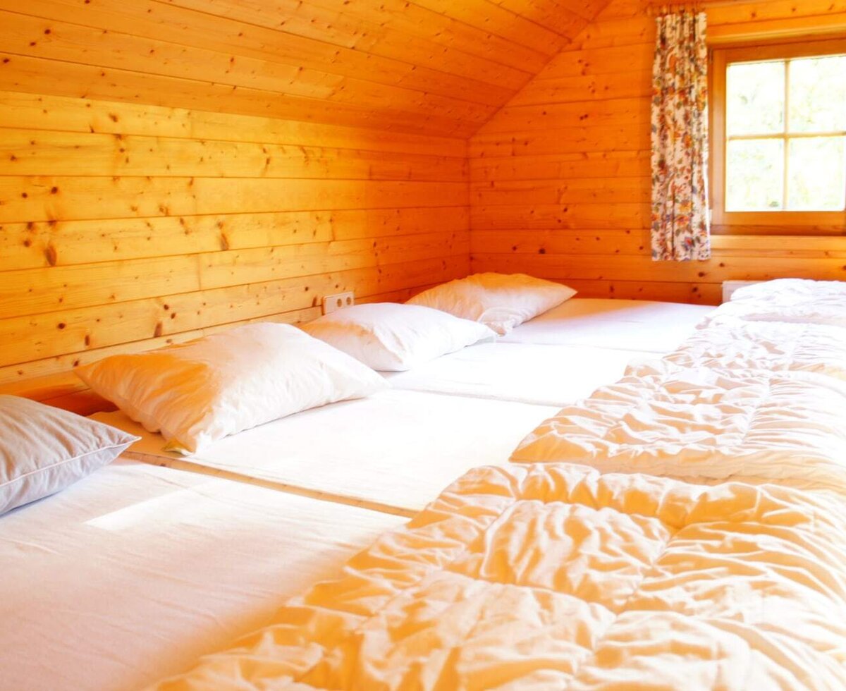 A multi-bed room in the farmhouse, featuring wooden paneling, white bedding, and a window.