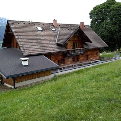 Our mountain cabin, a wooden building with a tiled roof, balcony, and surrounding grassy landscape.
