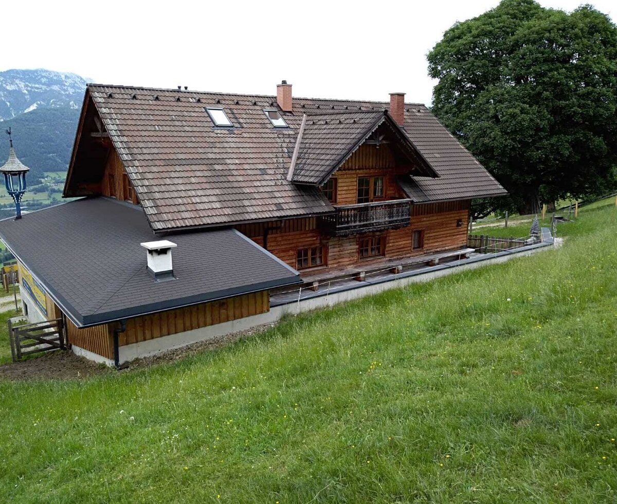 Our mountain cabin, a wooden building with a tiled roof, balcony, and surrounding grassy landscape.