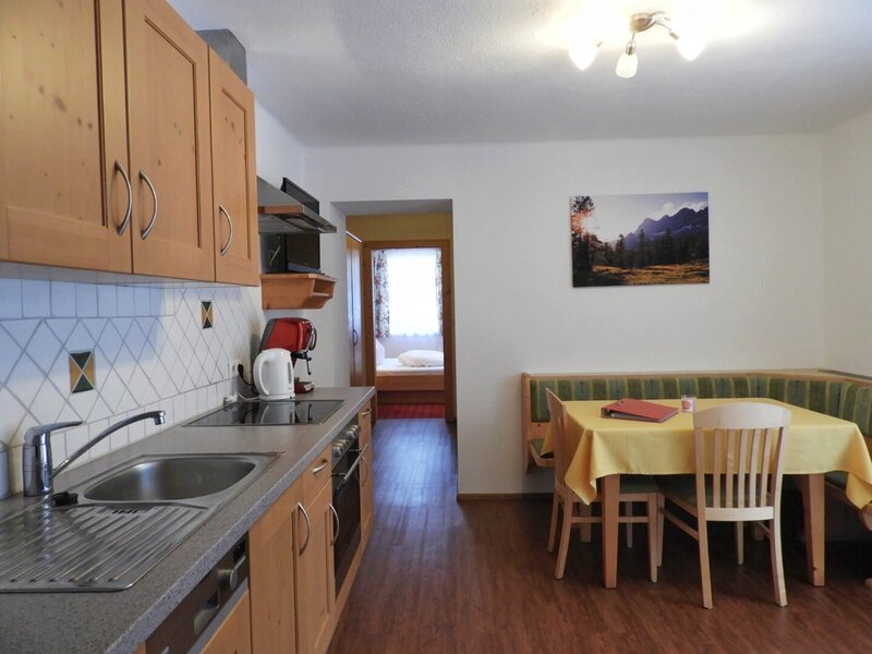 The fully equipped kitchen and dining area of the Farm House apartment, featuring a sink, stovetop, and coffee maker, with a dining table, bench seating, and access to a bedroom.