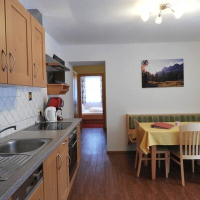 The fully equipped kitchen and dining area of the Farm House apartment, featuring a sink, stovetop, and coffee maker, with a dining table, bench seating, and access to a bedroom.