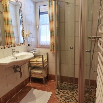 The Farm House bathroom features a shower cabin, a sink with a mirror, a heated towel rail, and shelves with fresh towels.
