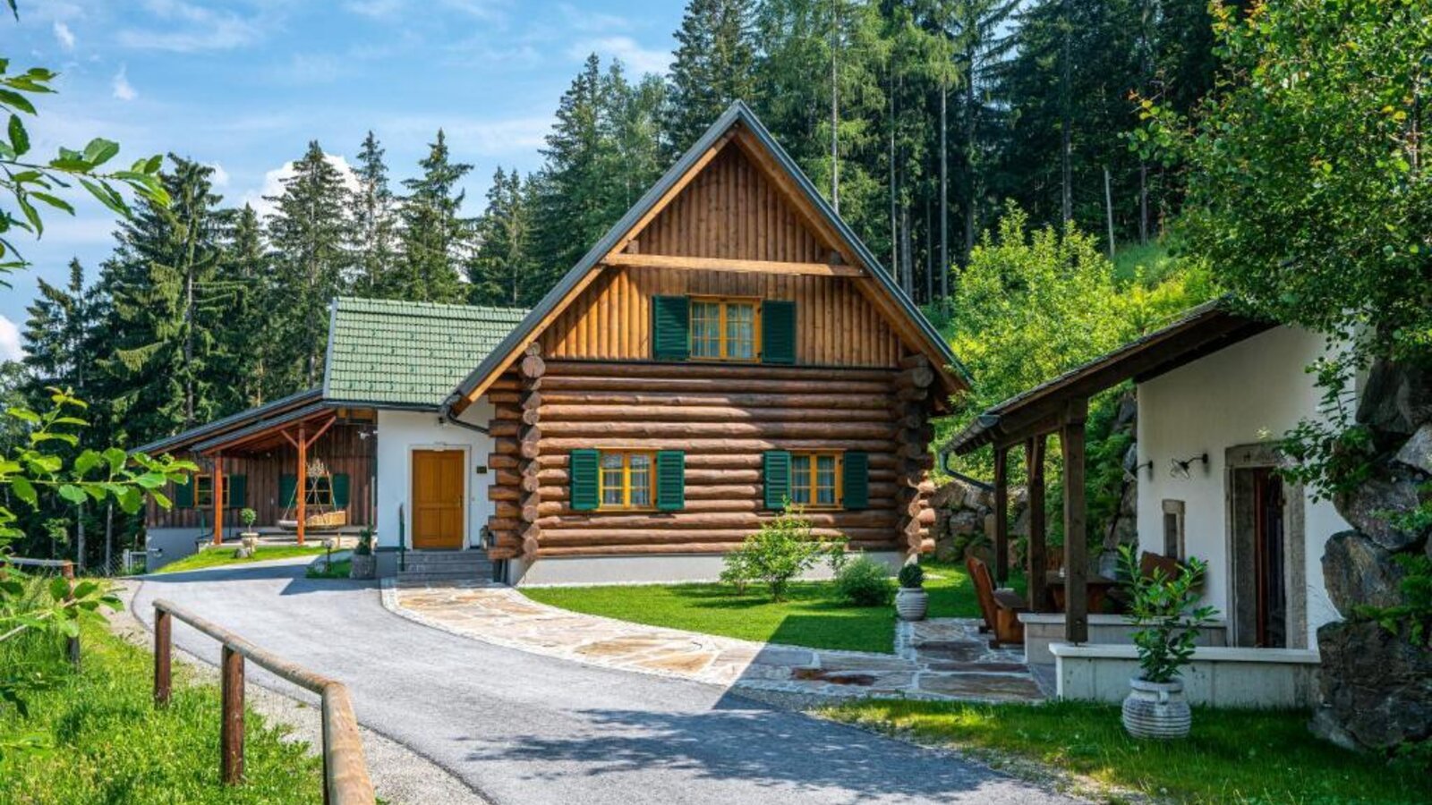 An inviting log cabin holiday home surrounded by lush forest and a well-manicured lawn.