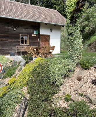Exterior of the hut with a wooden facade, white extension, and a terrace with a wooden table and benches.