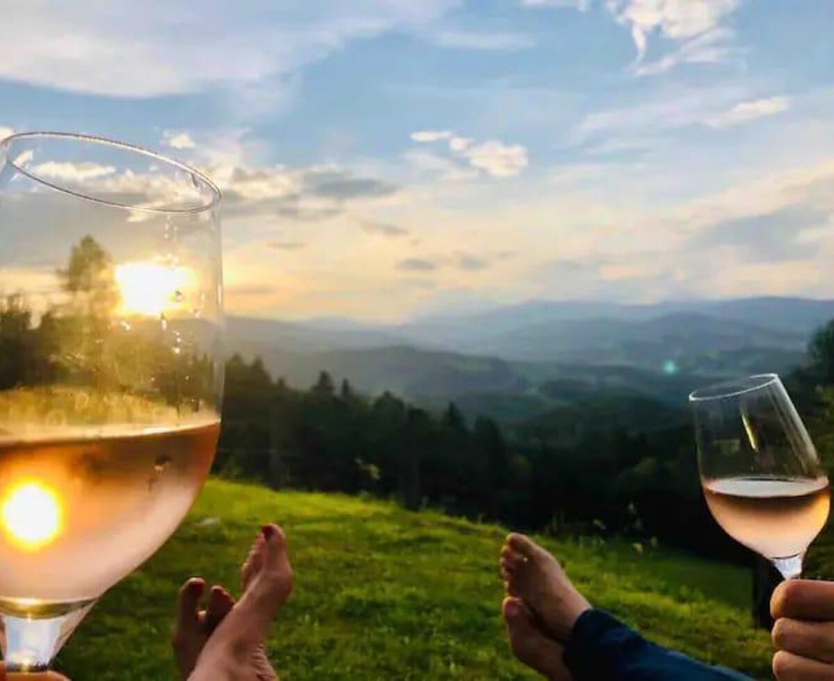 The farmhouse offers a sunset view of mountains, with two glasses of rosé wine and bare feet in the foreground.