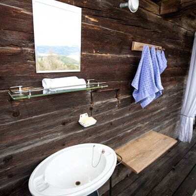 Outdoor wash station at the farmhouse with a sink, mirror reflecting the landscape, towels, and access to a balcony.