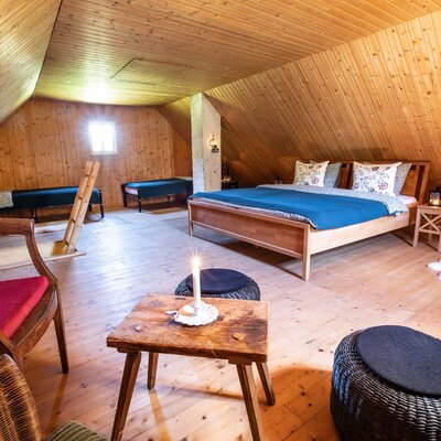 The attic bedroom in the farmhouse offers a double bed and multiple single beds, all within a wood-paneled space.