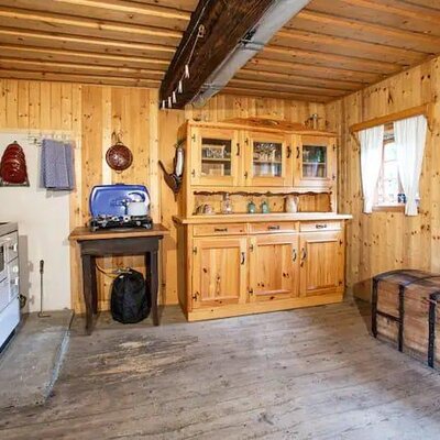 The farmhouse kitchen features a traditional wood-burning stove with an oven, a wooden hutch for storage, and a portable gas cooker on a side table.