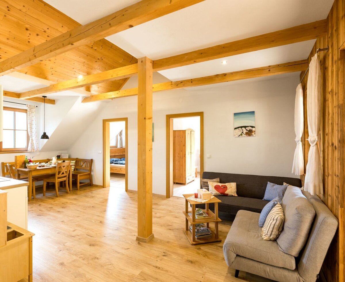 An inviting living area in the farmhouse featuring exposed wooden ceiling beams, comfortable sofas, and a rustic dining corner.