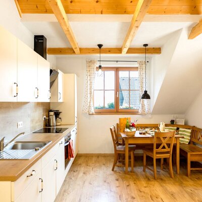 A bright kitchen-diner in the farmhouse, featuring a modern kitchenette, a cozy wooden dining area, and rustic ceiling beams.