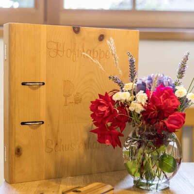 A warm welcome to the farmhouse, featuring a rustic wooden guest information binder and a fresh, colorful bouquet of flowers on the table.