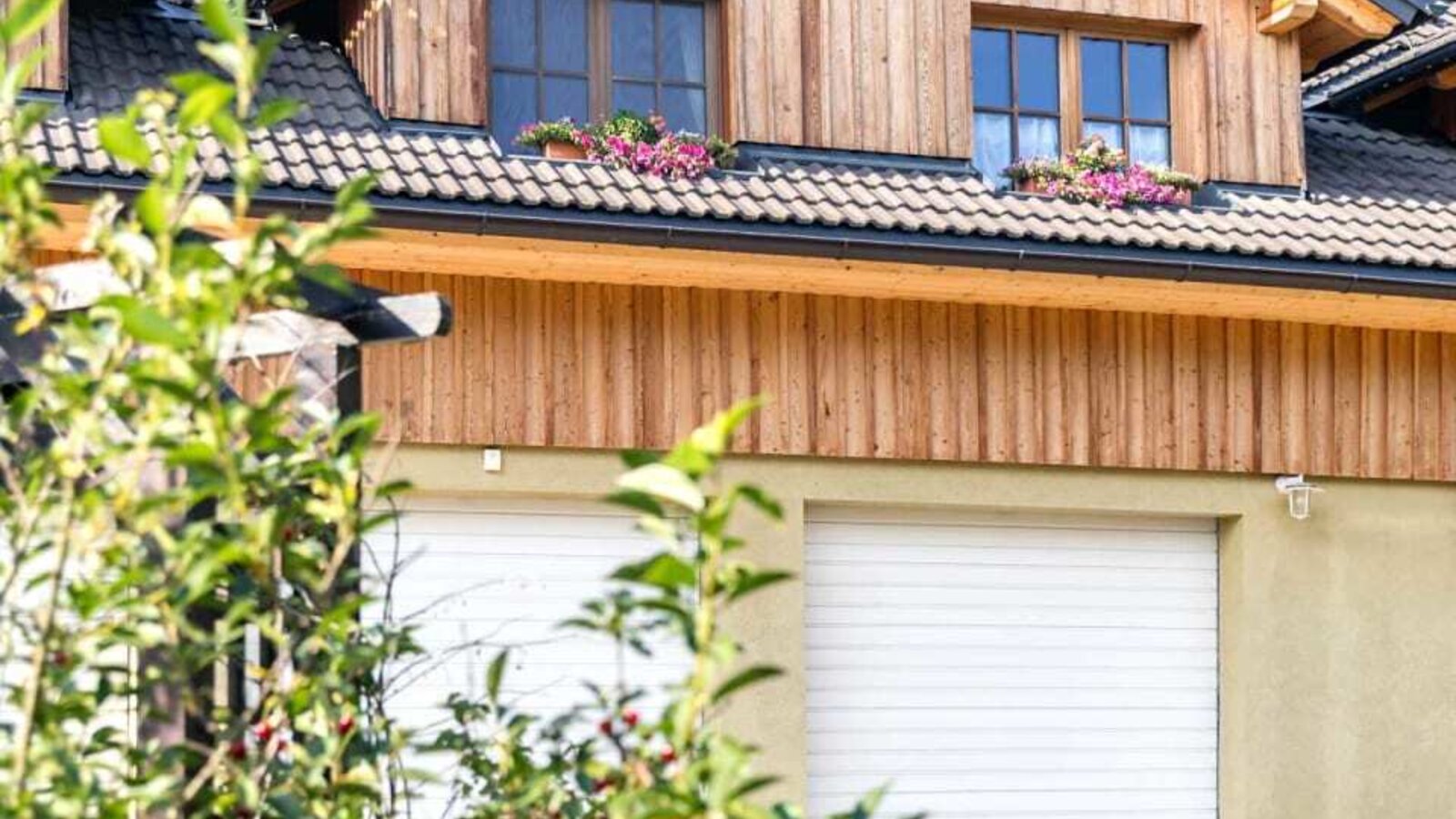 The farmhouse's inviting wooden facade featuring flower-adorned windows and lush green bushes in the foreground.