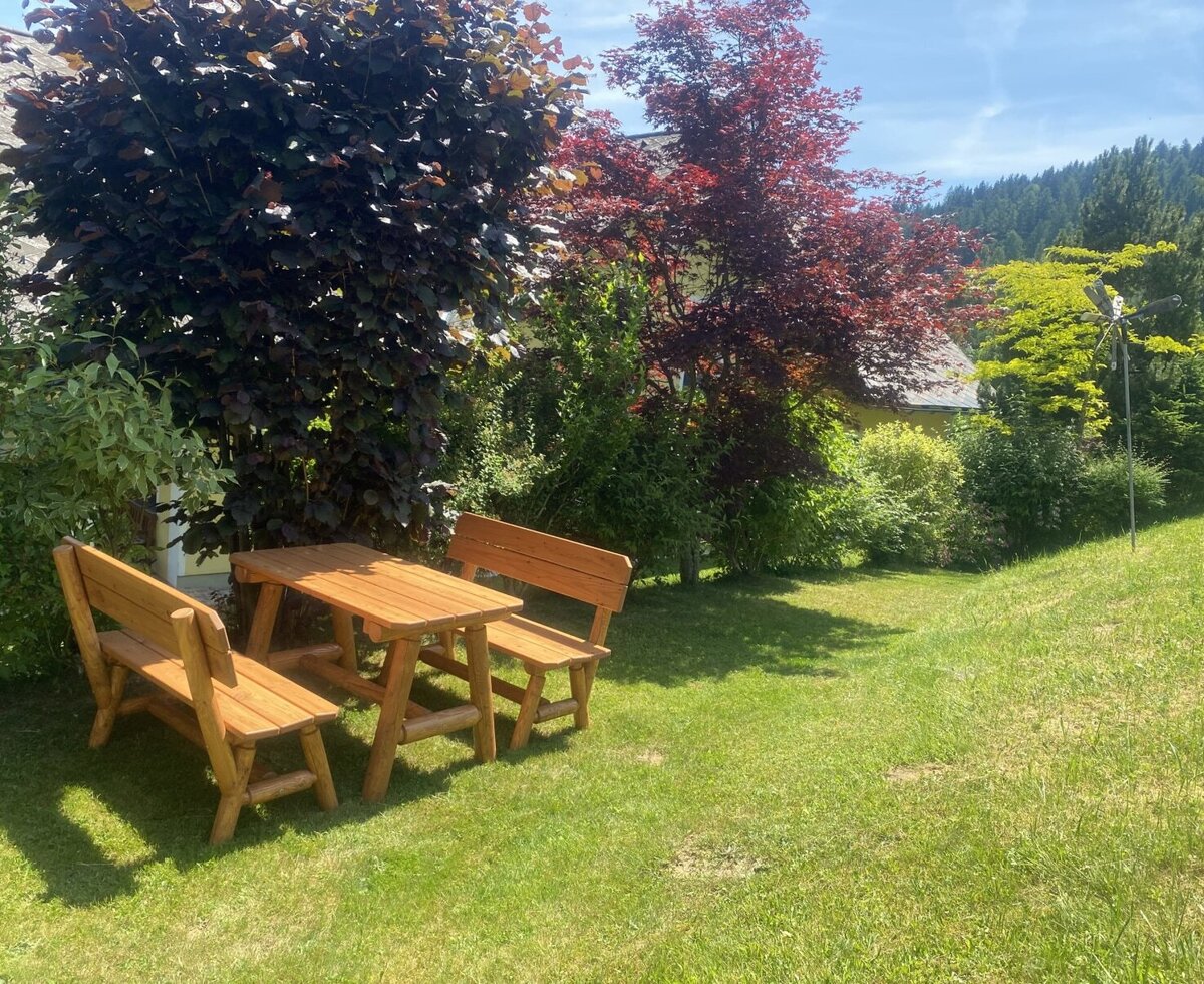 Outdoor seating area with a wooden table and benches on the farmhouse lawn.
