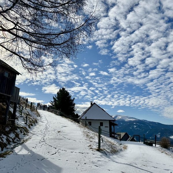 The exterior of the farmhouse on a snowy hillside with mountains in the background.
