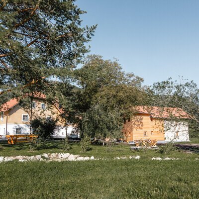 The exterior of the farm house and adjacent structures, set amidst a green lawn with a picnic table.