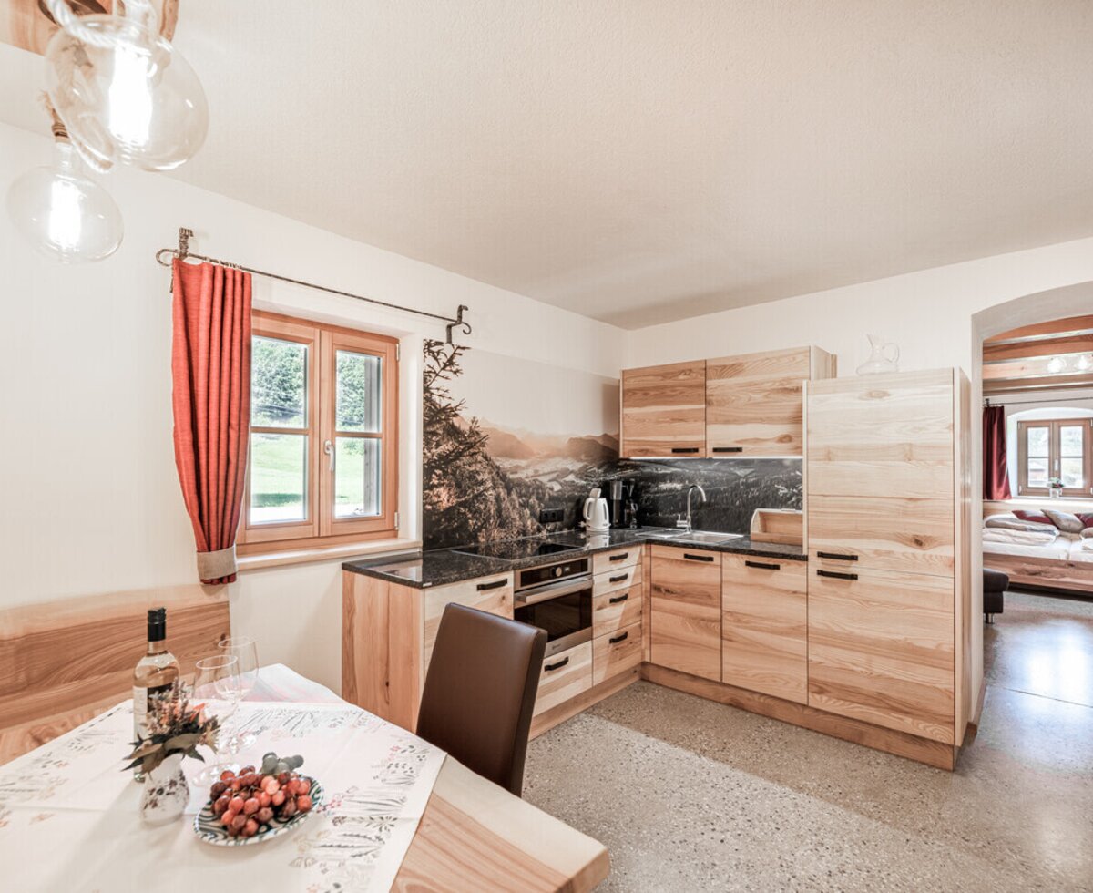 The farm house features a kitchen with wooden cabinets and built-in appliances, a dining area with a wooden bench, and an adjoining bedroom with two single beds.