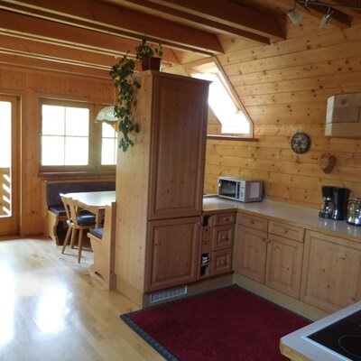 The farm house's fully equipped kitchen area, featuring wooden cabinetry, a stovetop, microwave, and coffee maker, next to a dining nook with direct balcony access.