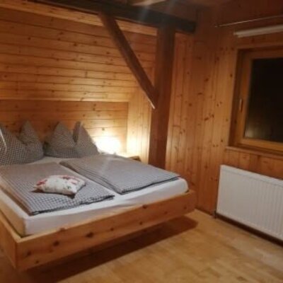 Double bedroom in the holiday house, featuring a high-quality arolla pine bed, wooden interior, and a window with a radiator.