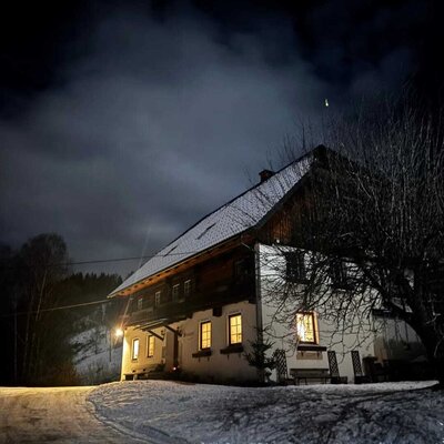 The inviting farmhouse at night, nestled in a snowy winter landscape with warmly lit windows.