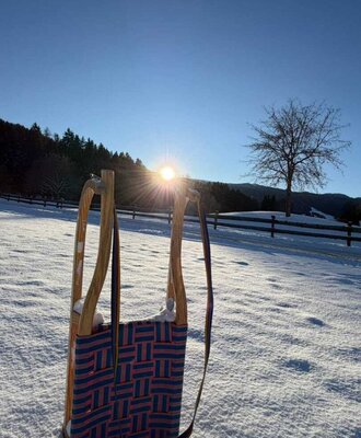 A traditional wooden sled in the glistening snow on the farmhouse grounds, beautifully lit by the low winter sun.
