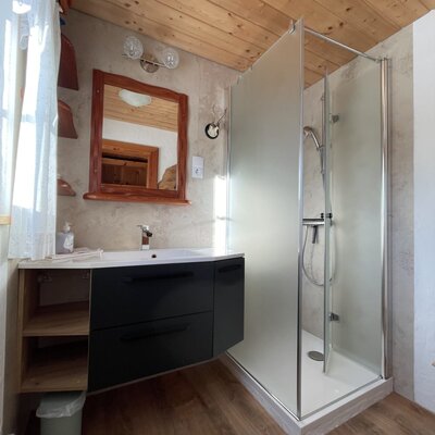 The farmhouse bathroom offers a shower cabin, a sink with a dark vanity unit, and a wooden-framed mirror.