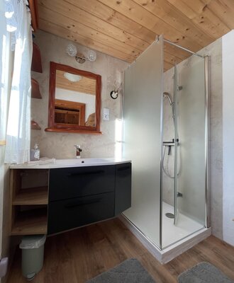 The farmhouse bathroom offers a shower cabin, a sink with a dark vanity unit, and a wooden-framed mirror.