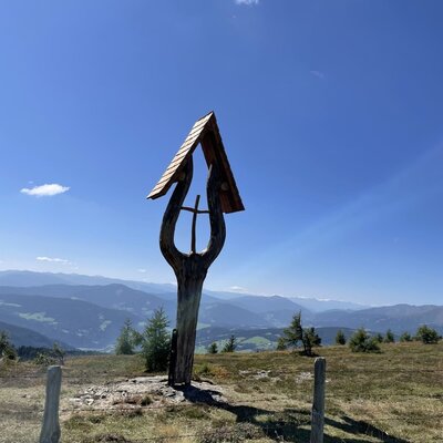 The surrounding mountain landscape with a wooden wayside cross near the farmhouse.