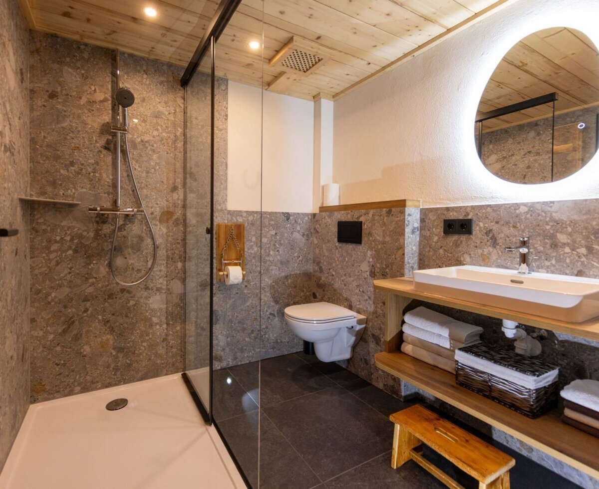 Bathroom in the farmhouse with a shower, toilet, sink, and illuminated mirror. (c) Hans-Peter Steiner