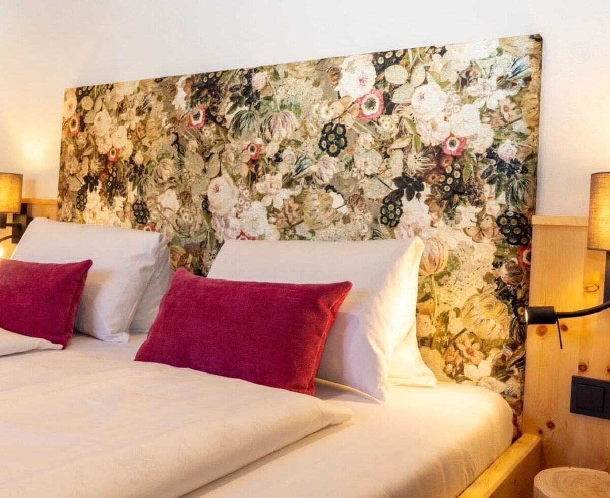 Bedroom in the farmhouse with a bed, floral headboard, wall lamps with reading lights, and wooden panels. (c) Hans-Peter Steiner