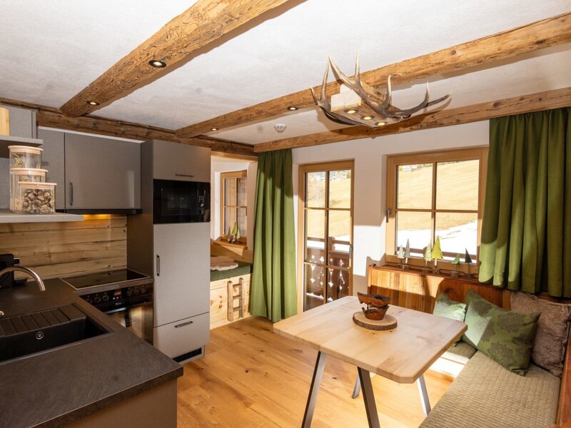 Kitchen and dining area in the farmhouse, featuring a modern kitchenette, dining table with bench seating, and windows with mountain views. (c) Hans-Peter Steiner