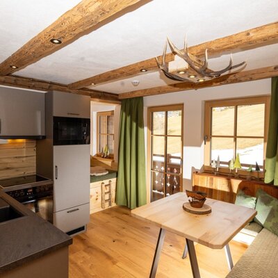 Kitchen and dining area in the farmhouse, featuring a modern kitchenette, dining table with bench seating, and windows with mountain views. (c) Hans-Peter Steiner