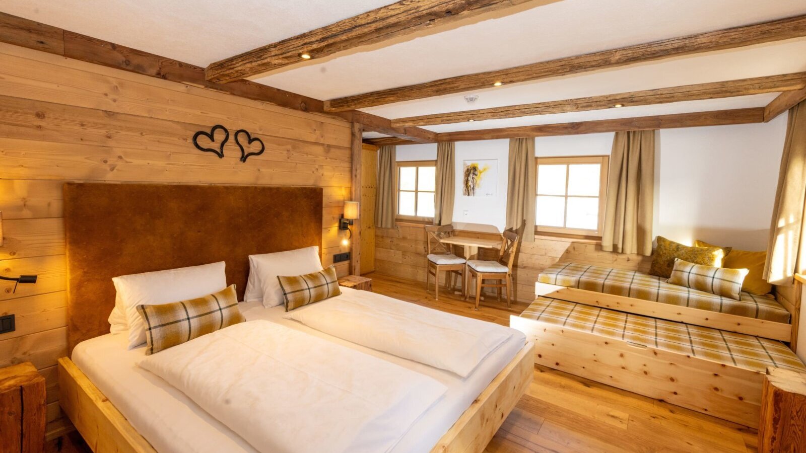 Bedroom in the farmhouse with a double bed, daybed, wooden furnishings, and a small table with chairs. (c) Hans-Peter Steiner