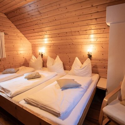 Bedroom in the upper flor with family-bed, wooden walls, a small window and an armchair.