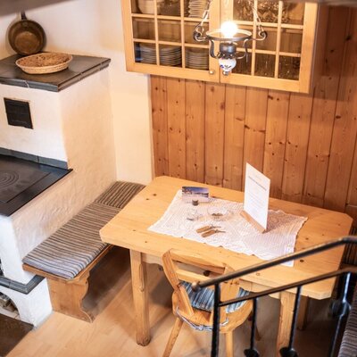 Dining area in the Troadkasten featuring a wooden table, bench, chair, and a traditional wood-burning stove.