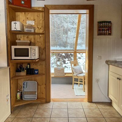 The kitchen of the Ap­par­te­ments, featuring a microwave, toaster, and access to the winter garden with a view of the snowy landscape.