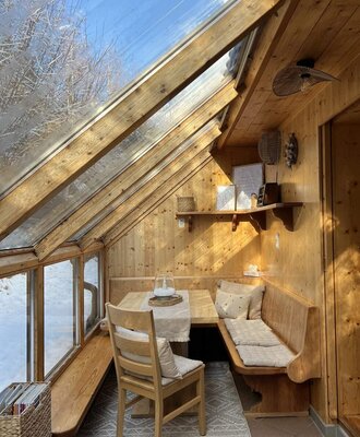 Winter garden of the Appartements with a dining table, bench seating, and a view of the snowy landscape.