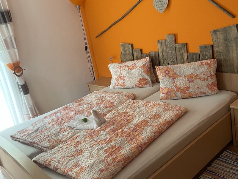 Double bedroom in the Farm House, featuring a wooden headboard, an orange accent wall with decorative rakes, and sheer curtains by the window.