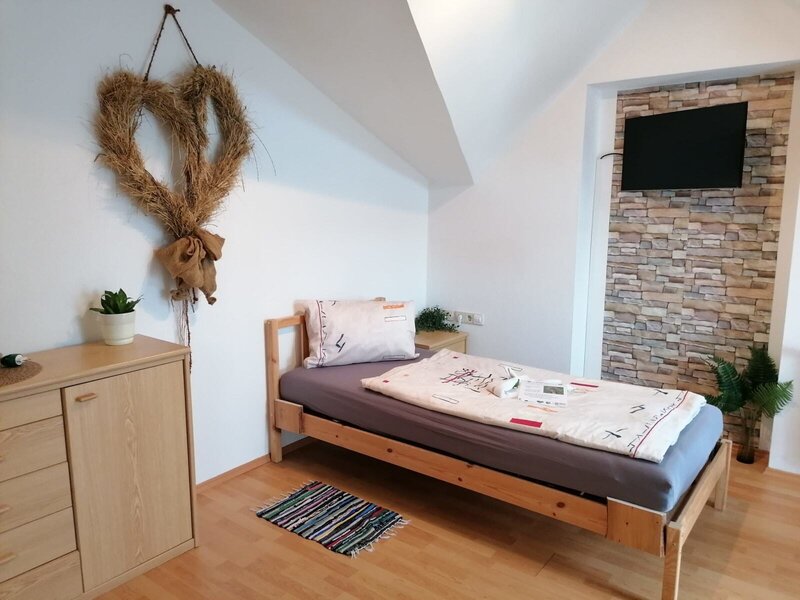 Single bedroom in the farmhouse featuring a wooden bed, wall-mounted satellite TV, and a wooden dresser.