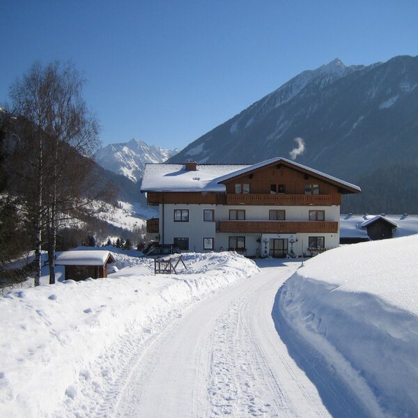 The snow-covered Farm House exterior features balconies, an access path, and mountains in the background.