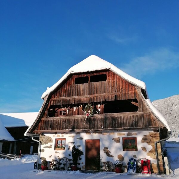 The farm house exterior, covered in snow, features a whitewashed stone base and a wooden upper level with an open balcony.