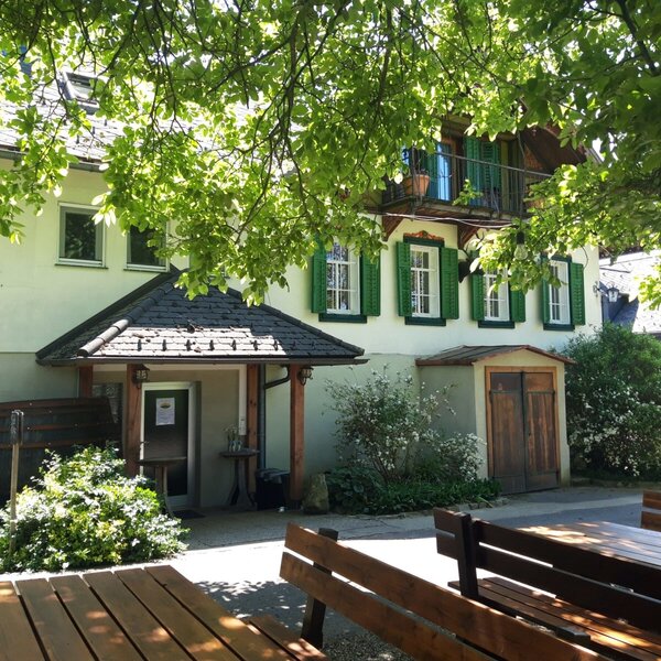 The exterior of the farmhouse with green-shuttered windows, a covered main entrance, a balcony, and wooden picnic tables for outdoor seating.