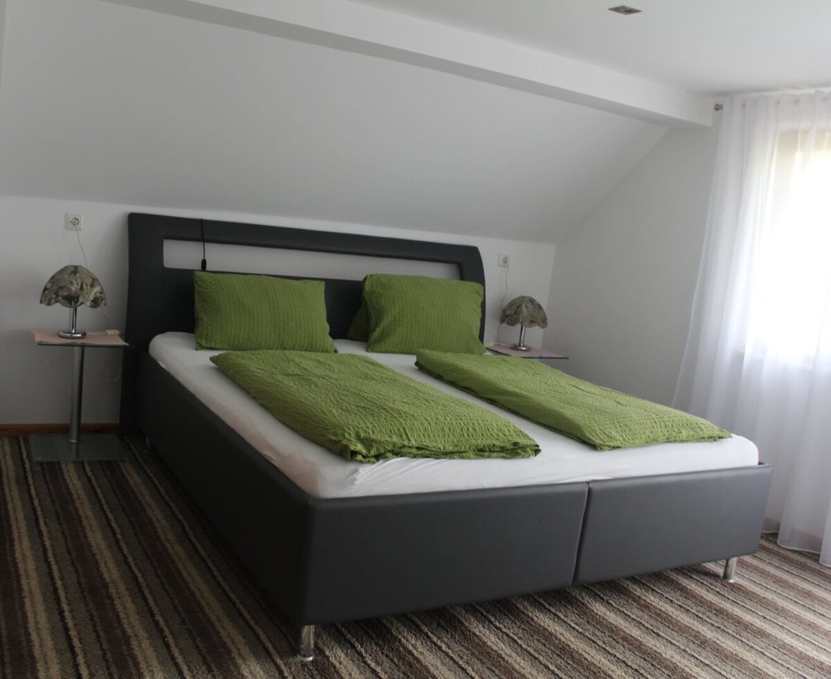 Double bedroom in the farmhouse featuring a bed with green bedding, two bedside tables with lamps, and a window with sheer white curtains.