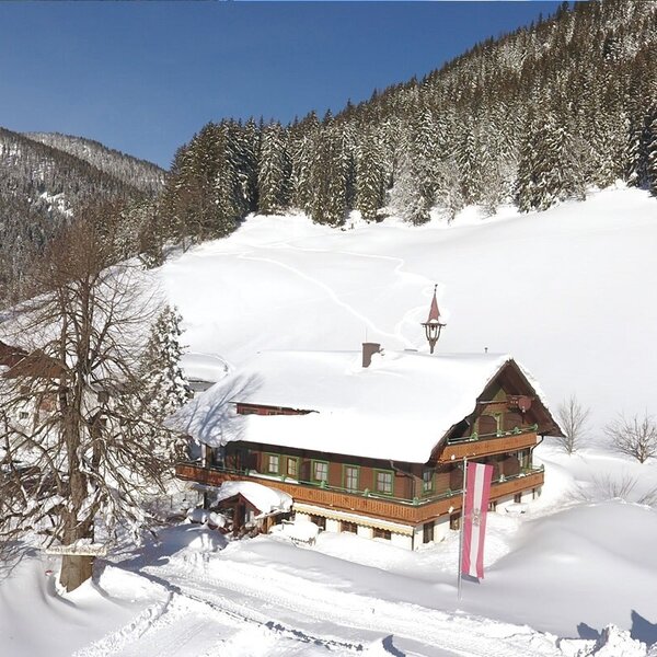 The Farm House in winter, featuring snow-covered roofs and balconies, set against a backdrop of snow-dusted mountains and pine forests.