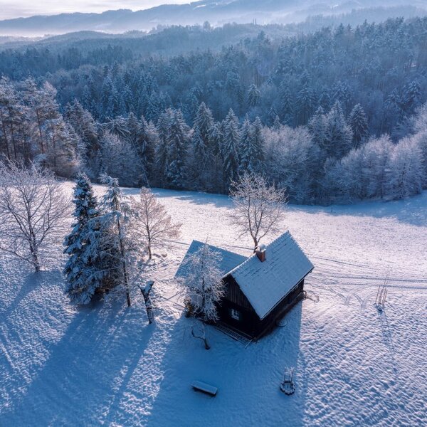 The farmhouse in a snow-covered meadow with a forest and hills in the background. The farmhouse in a snow-covered meadow with a forest and hills in the background.