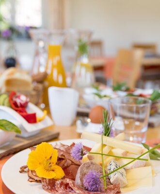 Breakfast at the farmhouse, featuring a plate with cold cuts, various cheeses, pâté, and edible flowers. (c) Elisabeth Fröhlich Photography