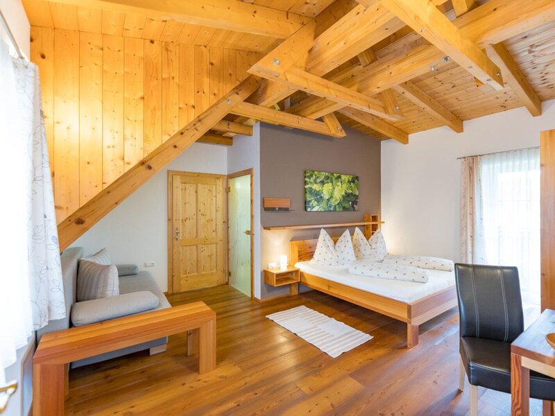Double room in the farmhouse with a wooden beamed ceiling, double bed, sofa, and dining area. (c) Elisabeth Fröhlich Photography