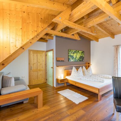 Double room in the farmhouse with a wooden beamed ceiling, double bed, sofa, and dining area. (c) Elisabeth Fröhlich Photography