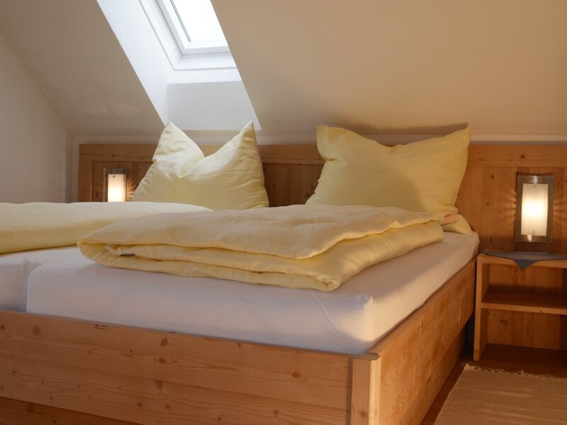 Farmhouse bedroom equipped with two single beds, wooden headboards with integrated lights, a bedside table, and a skylight.