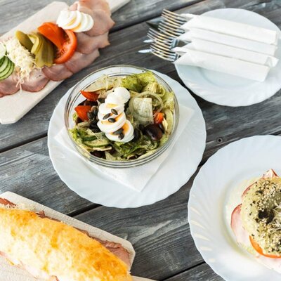 A selection of dishes on a wooden table, including a cold cut platter with vegetables and eggs, a salad, and various sandwiches, served at the Haus.